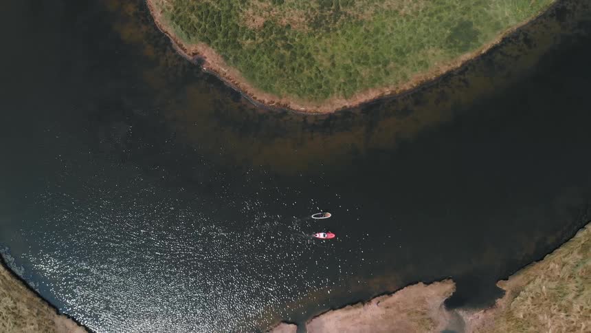 Two people paddle down a stream