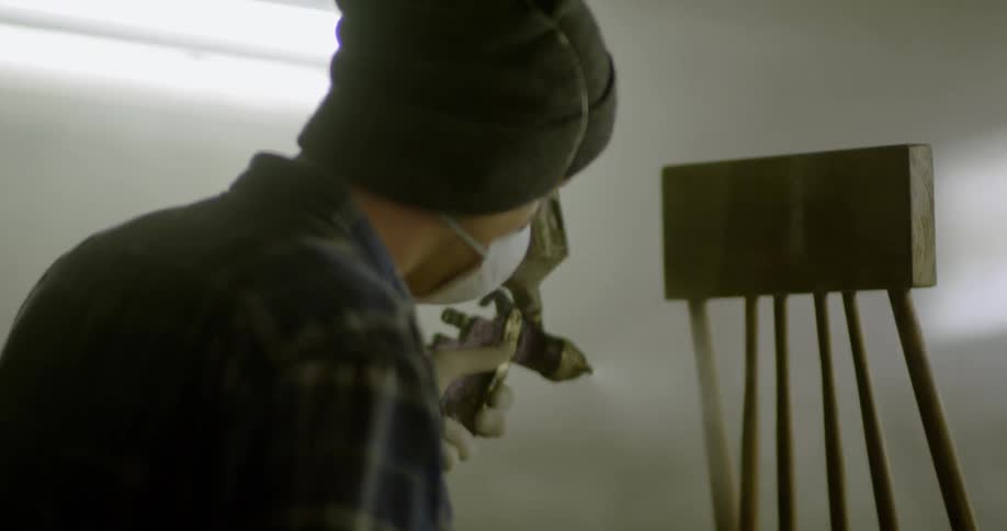 A painter sprays paint on a piece of wood