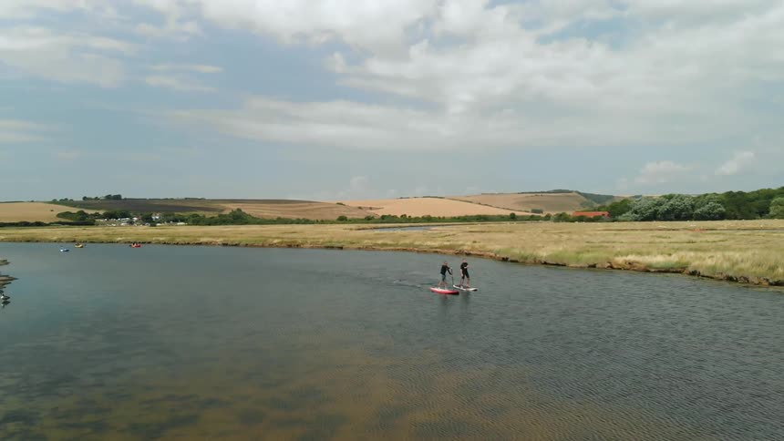 Two people paddle board down a stream
