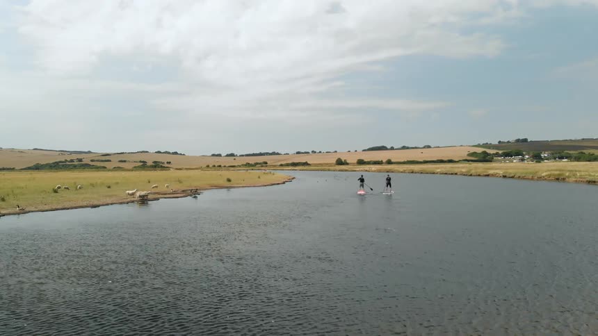 Two people paddle board down a stream