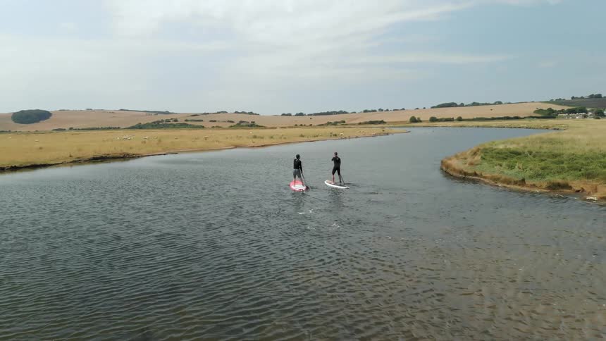 Two people paddle board down a stream