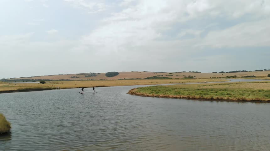 Two people paddle board down a stream