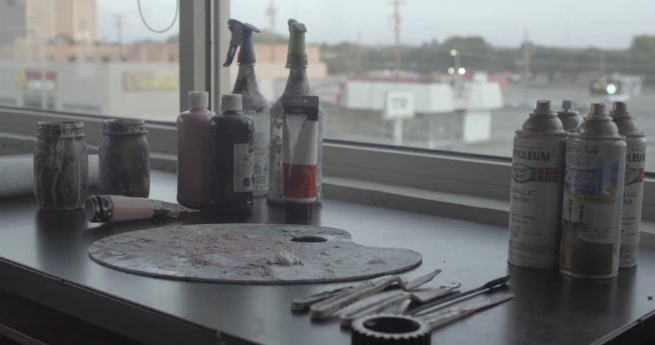 An artists palette sits atop a counter by jars and cans of paint