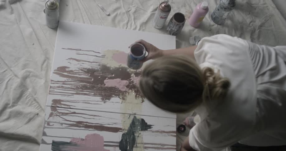 A woman is pouring paint onto a work of art she is making