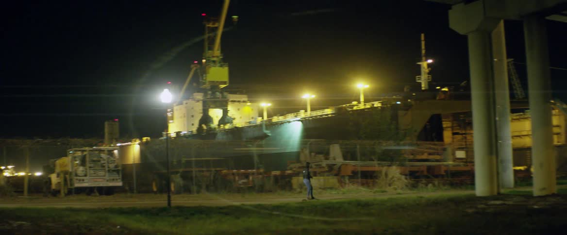 A skateboarder rides by an industrial building at night