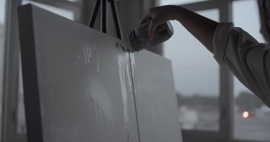An artist pours paint on a canvas