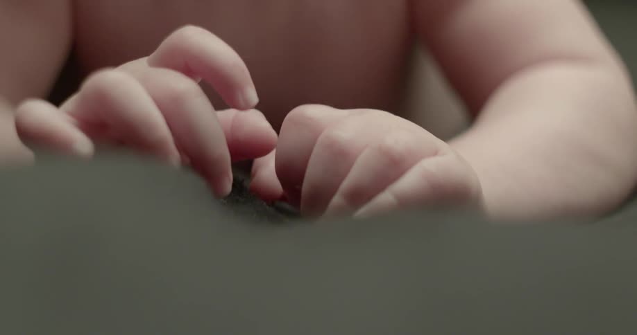 A baby with small hands and no shirt is filmed up close