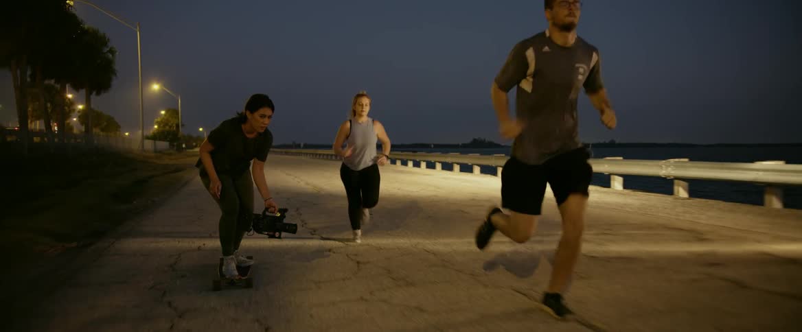 A woman on a skateboard films two joggers running