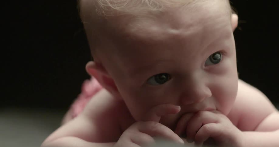 An infant lays and sucks on its fingers