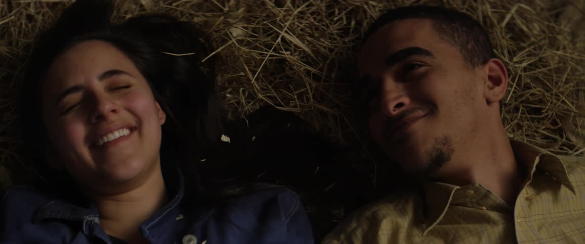A couple smile and laugh as they lay on a pile of hay