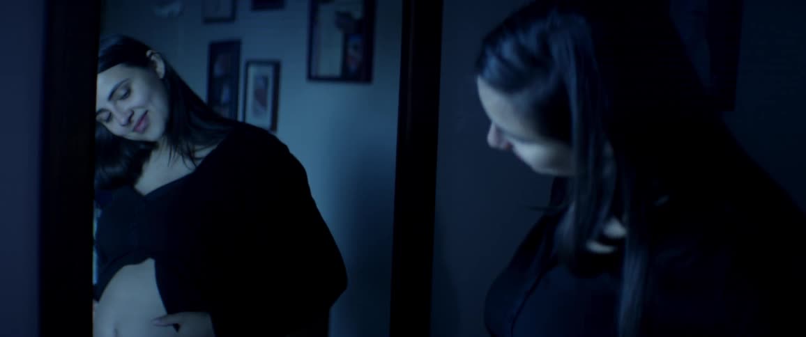 A young woman looks at her pregnant belly in a mirror