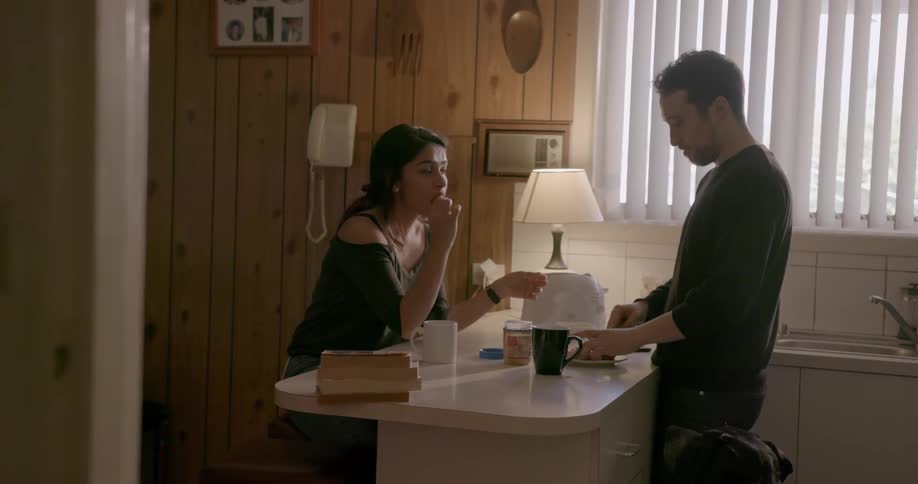 A man and woman drink coffee at a kitchen counter