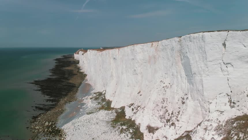 A white cliff towers over an ocean shore