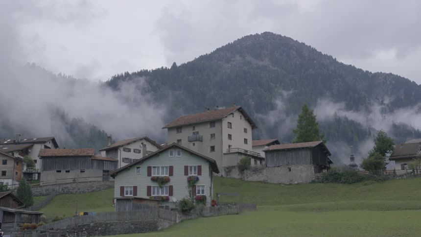 Small village sitting before mountains with clouds hovering around
