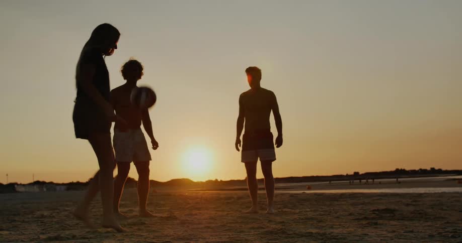 Four adults kicking a ball in the sand at sunset