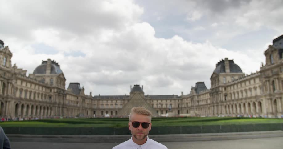 Man puts on sunglasses standing in front of a large building
