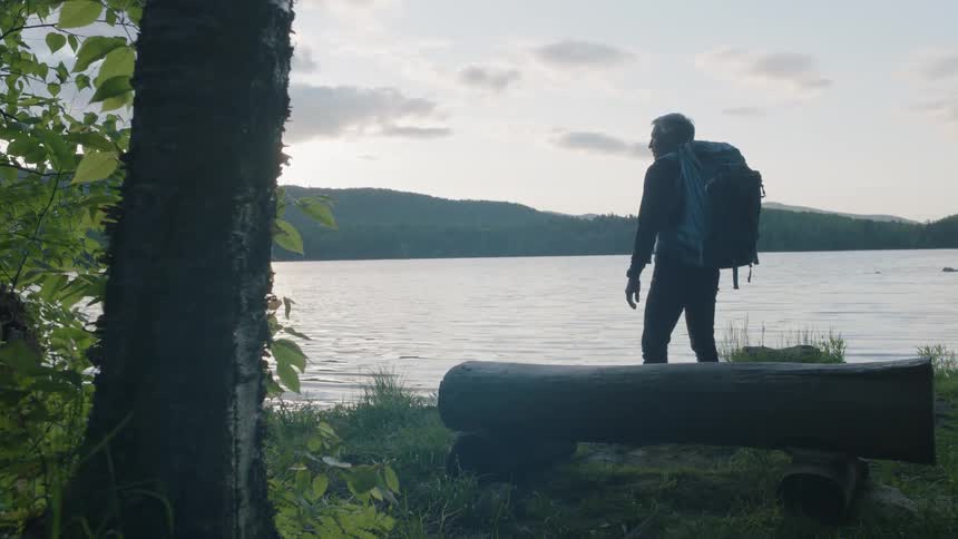 A backpack wearing man stands near a log