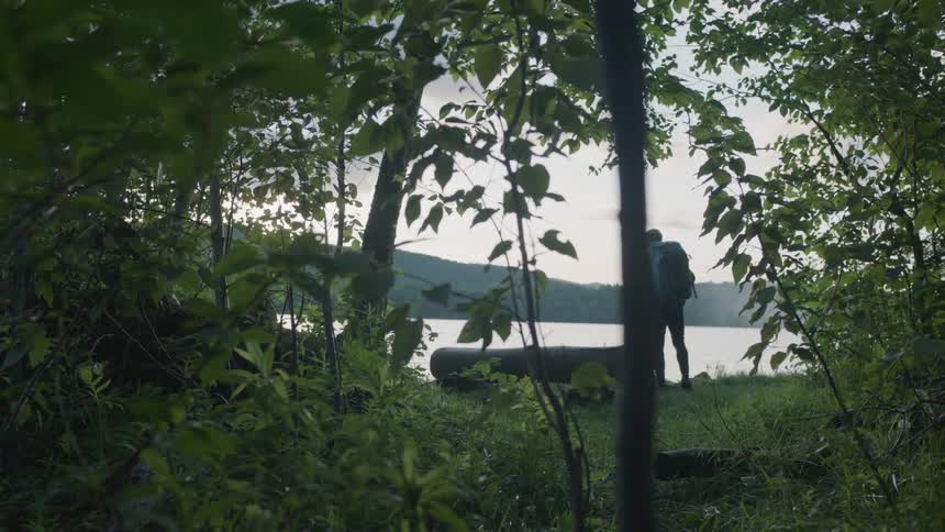 A backpacker stands near a lake