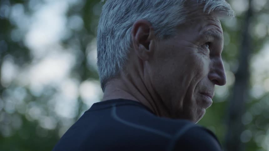 Elderly man stands outside near trees
