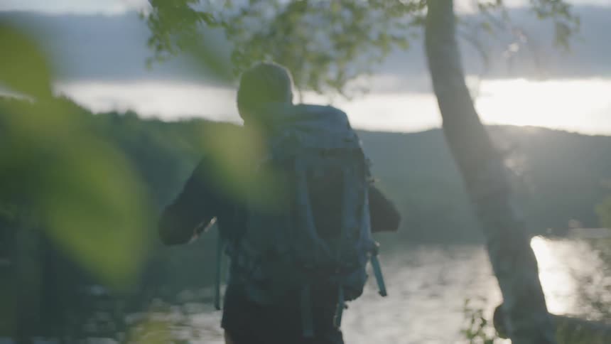 A man with a backpack is standing next to a river
