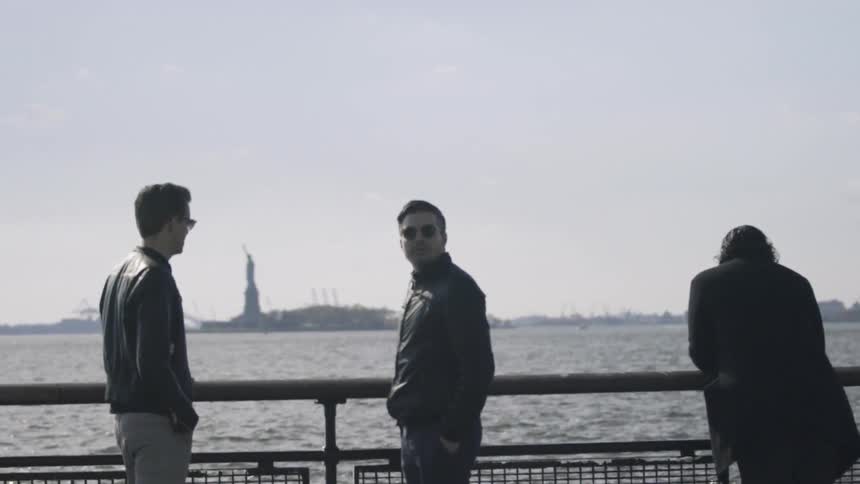 Three men stand with the statue of liberty in the distance