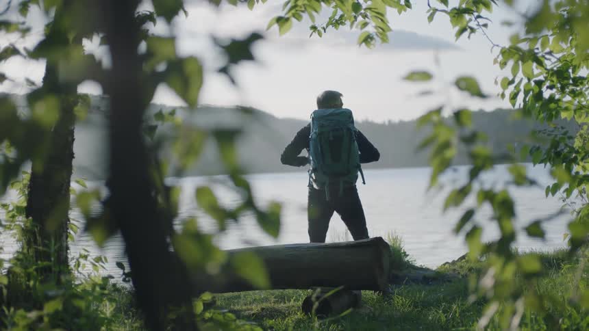 Man wearing a backpack looks out across the water