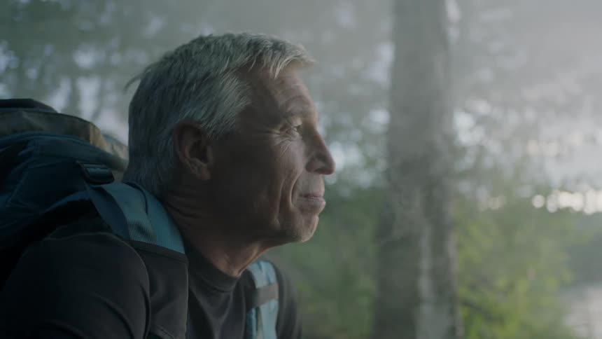 Man with backpack sits on mountain slope smiling