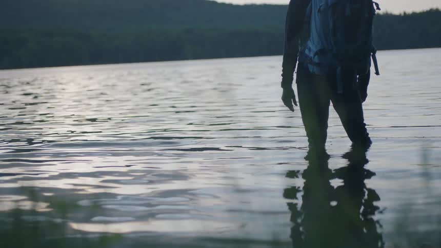 Hiker stands knee deep in a mountain lake