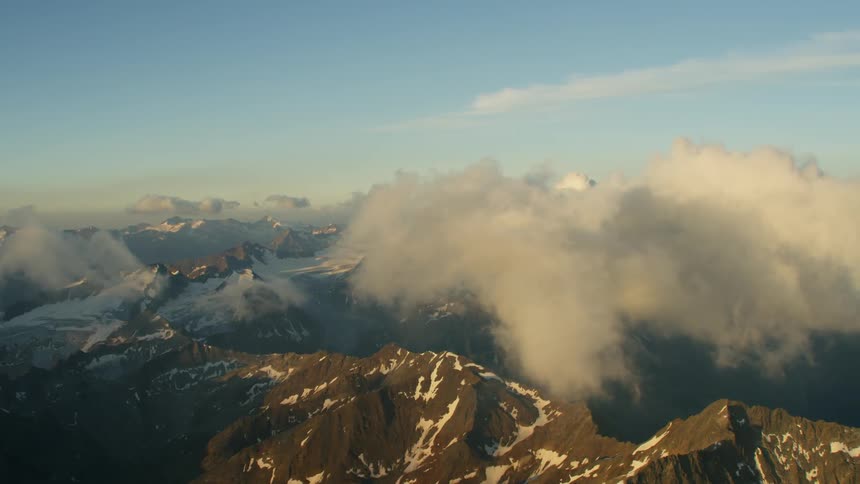The large mountain range has ice at the top of some parts at sunset