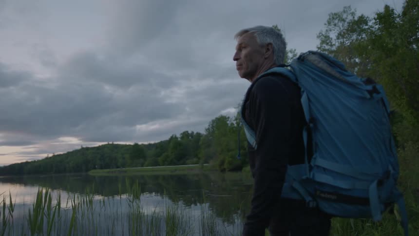 Hiker stands next to a mountain lake at sunset