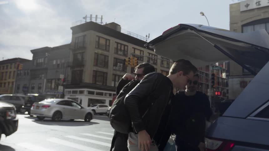Men unload bags from a vehicle parked on a city street