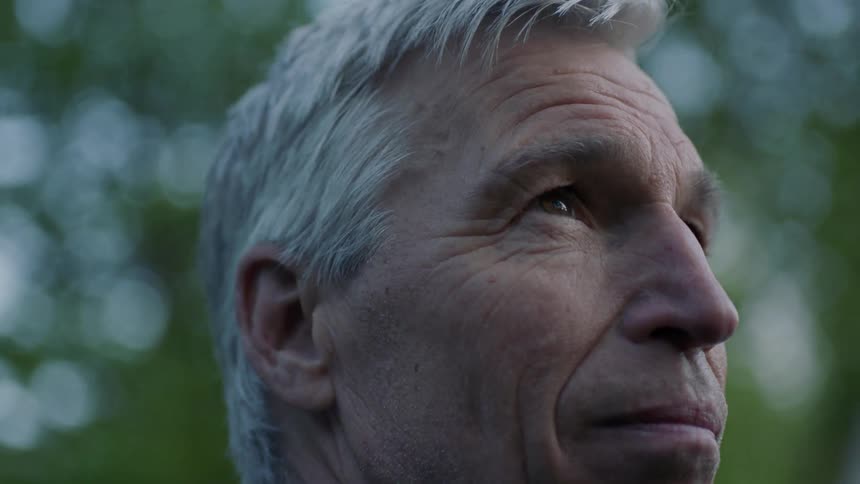 Elderly man stands near trees