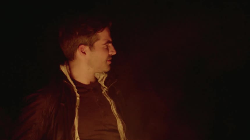 Man talks while standing next to a bonfire at night