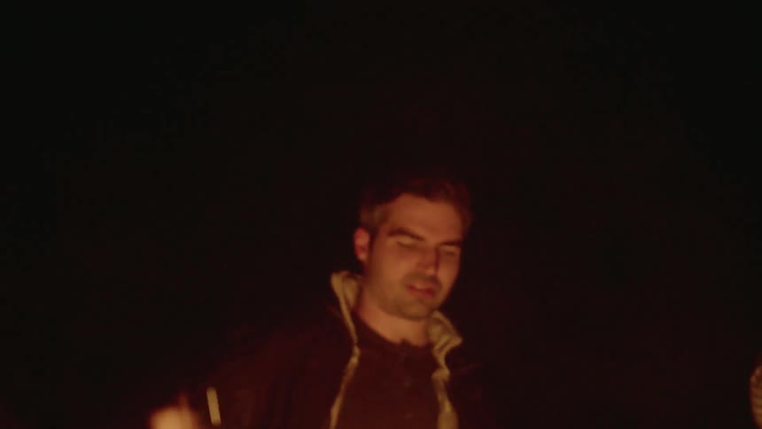 Man stands next to a bonfire at night