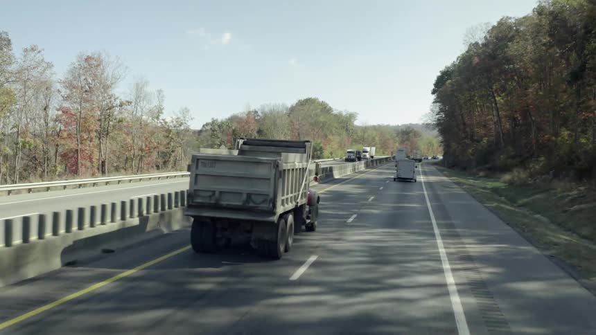 A dump truck travels with traffic on a rural highway