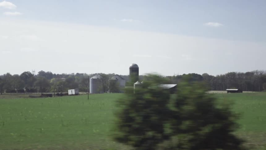 A vehicle drives by a farm on a rural road