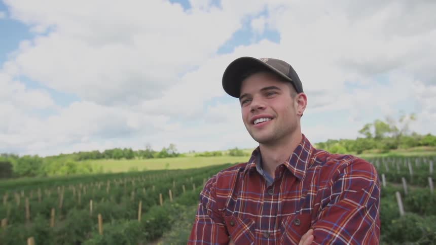 A man in a plaid shirt and hat is standing on a farm