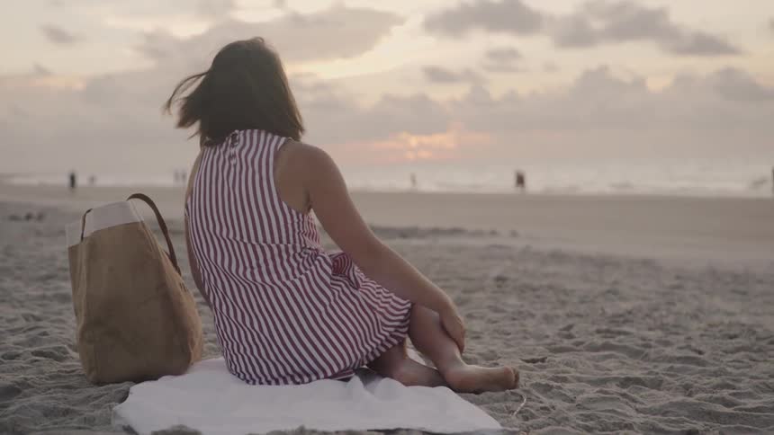 Woman sits on a towel on a beach at sunrise