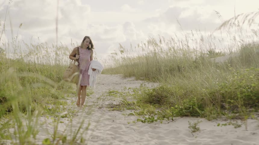 A woman walks down a trail on the beach