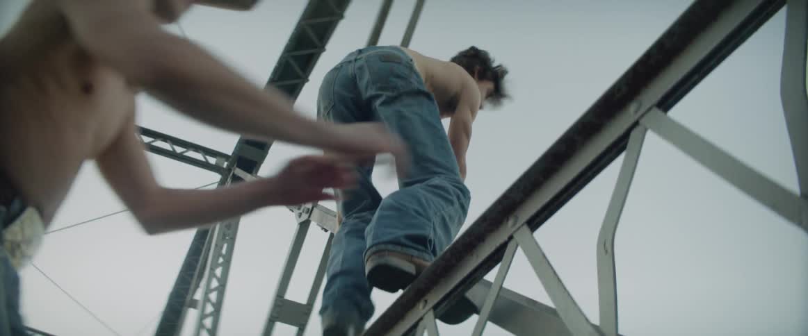 Two young men climb high on a bridge at dawn, confident and fearless