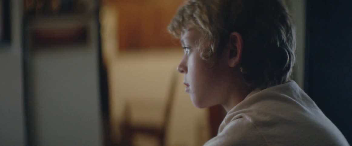 A young boy watches television in profile, lit by its flickering glow