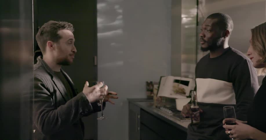 A group of people converse in a kitchen at a party
