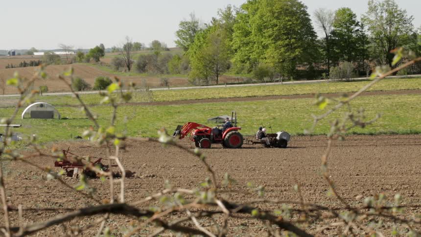 A tractor tills soil on a farm on a sunny day