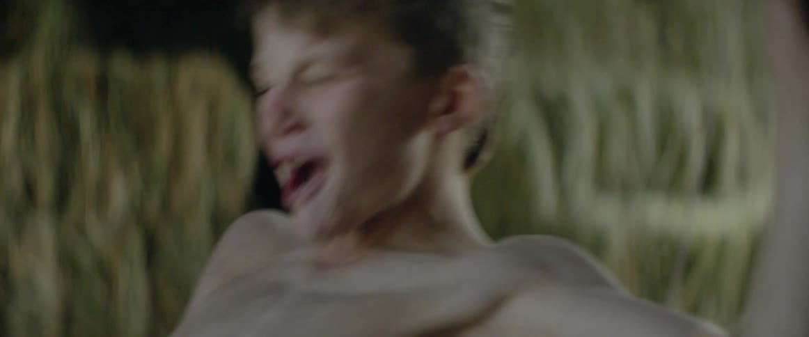 A young boy mimics riding a bull in a barn