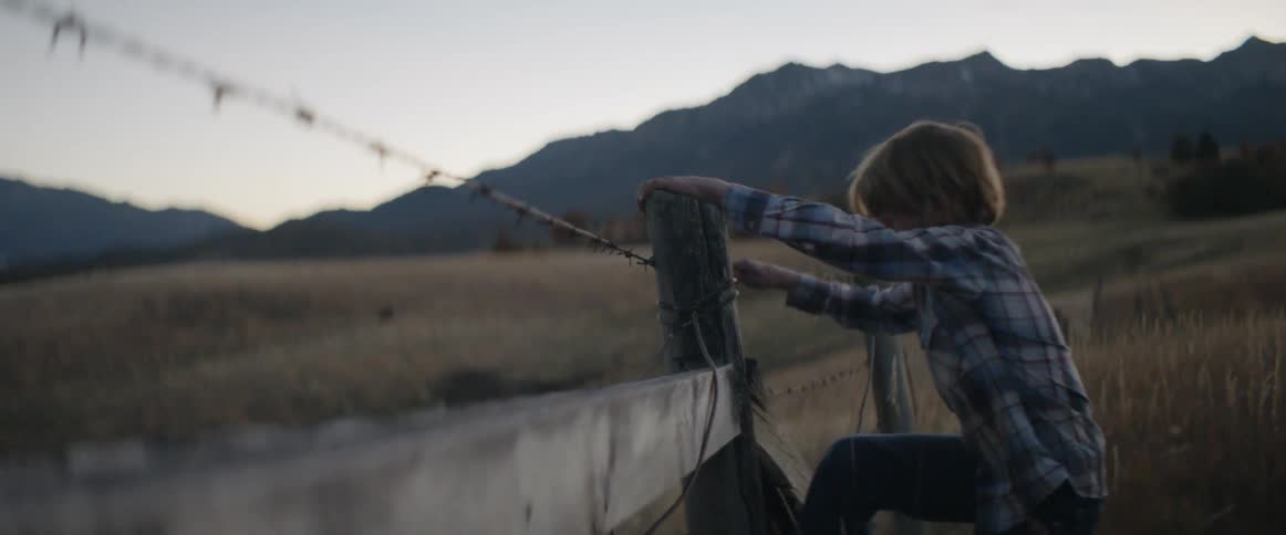 Two young boys climb over a barbed wire country fence