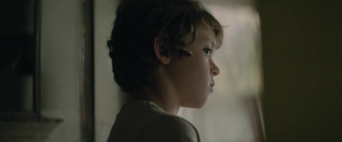 A young boy peeks around a corner indoors