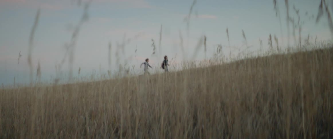 Two children run through a grass field