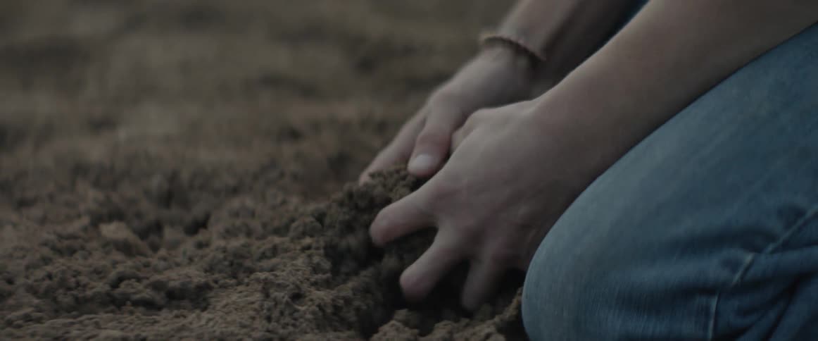 A person picks up a handful of dirt and squeezes it