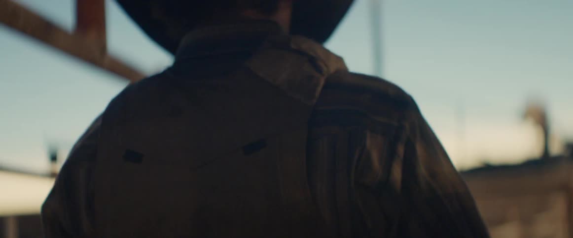 A cowboy walks by a gate at sunset