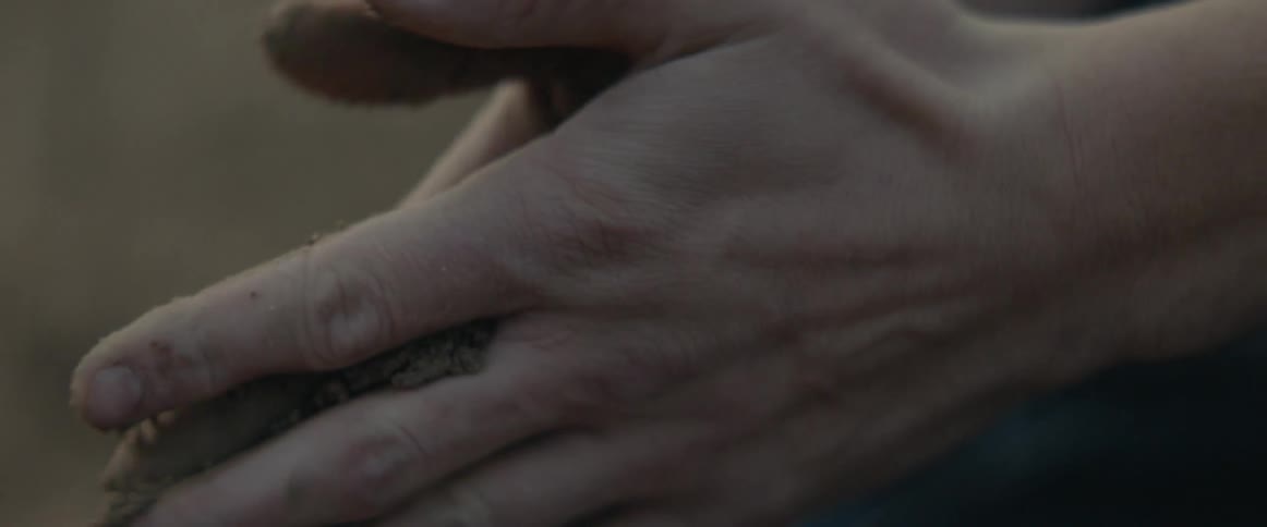 A man cups and rubs dirt from the ground